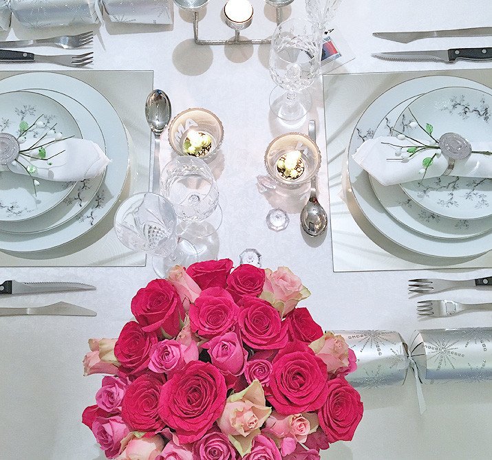table setting with pink roses and white tablecloth