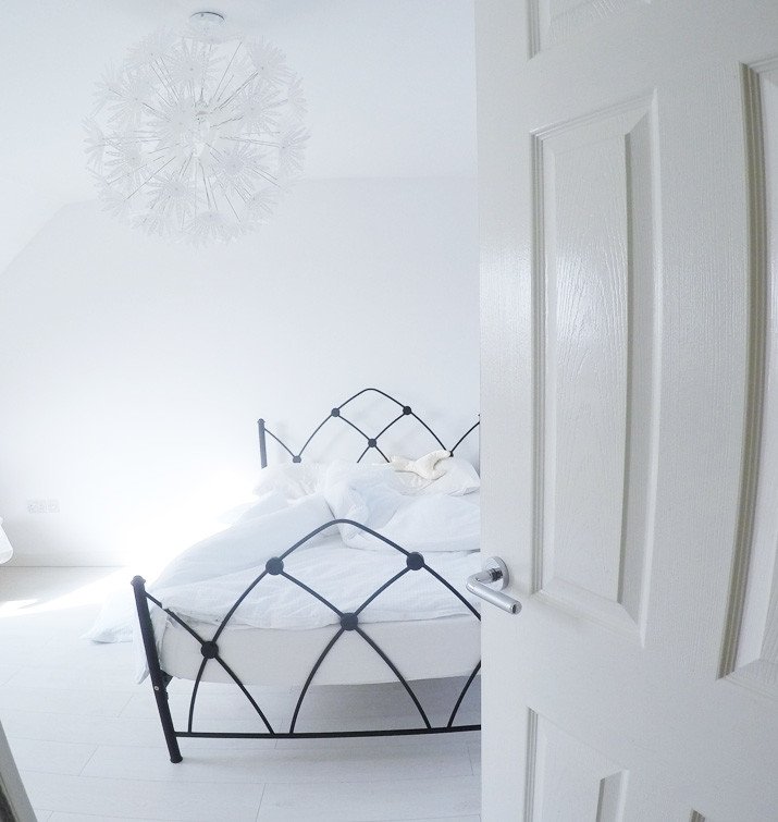 unmade bed in all-white bedroom