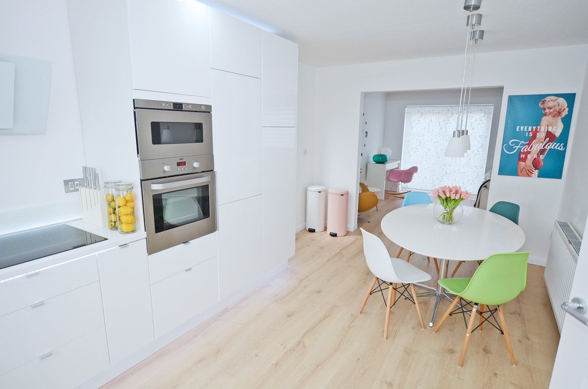 All-white Kitchen with Integrated appliances and multicoloured Eames chairs