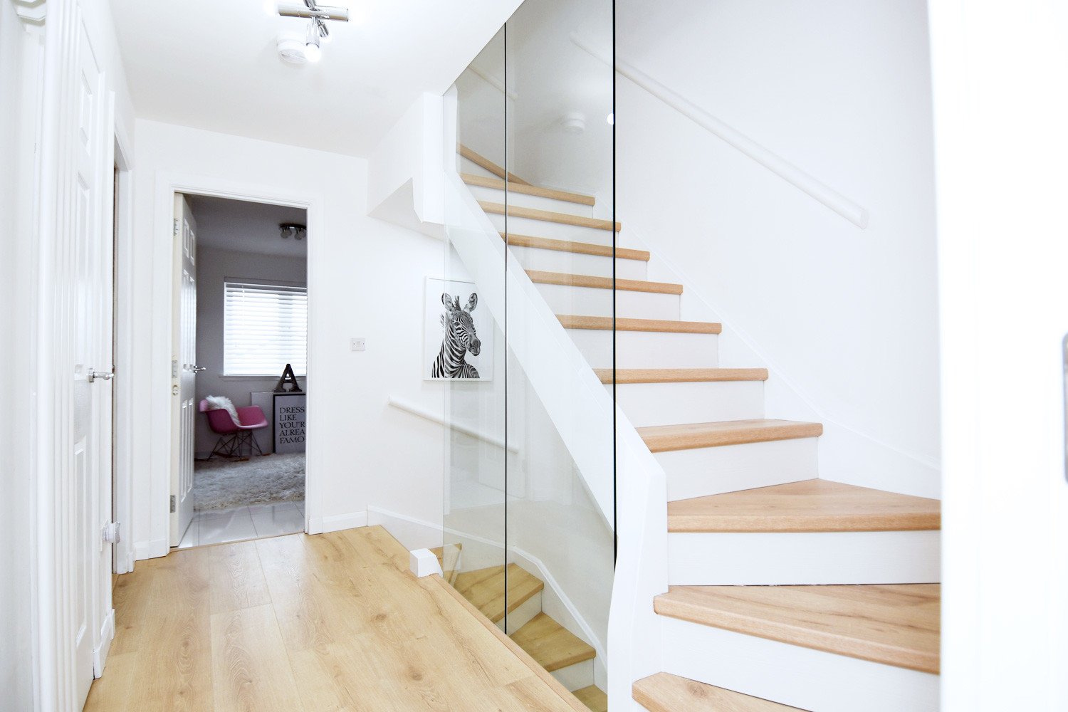 upstairs hallway with glass wall on the stair and pale wood floor