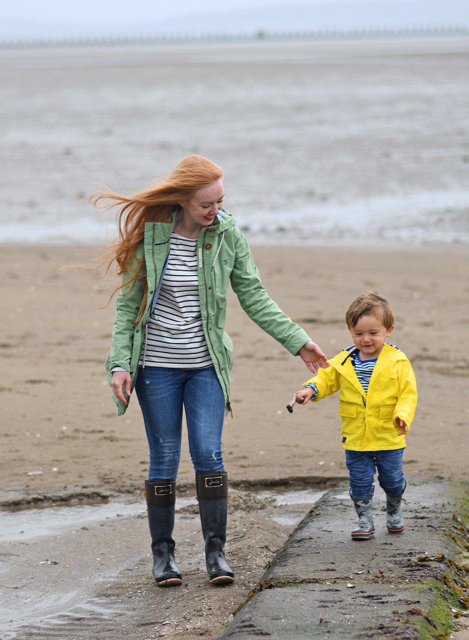 Mum and toddler on the beach in raincoats and wellies