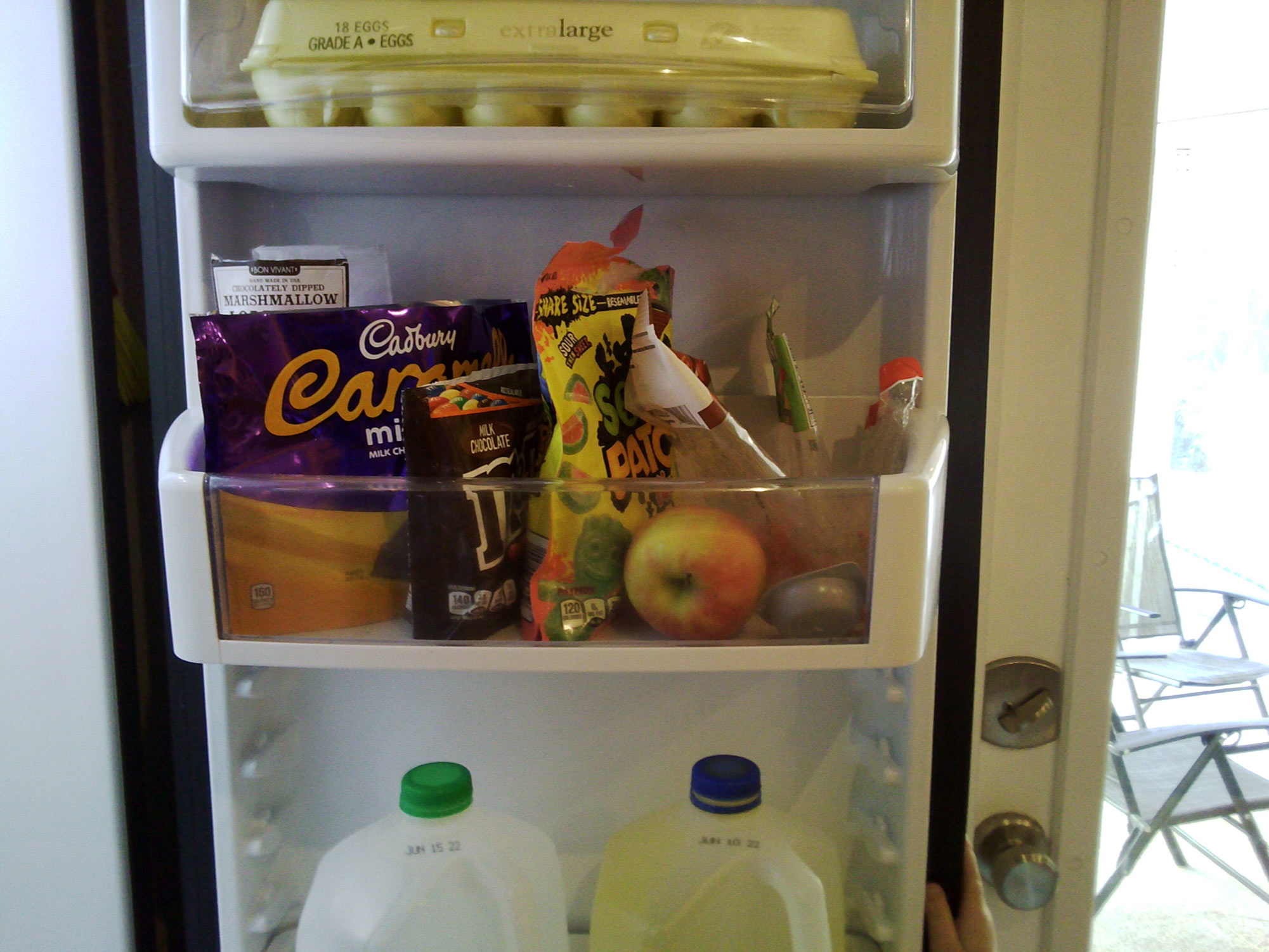 The inside of a fridge door, showing lots of sugar y snacks and a single apple