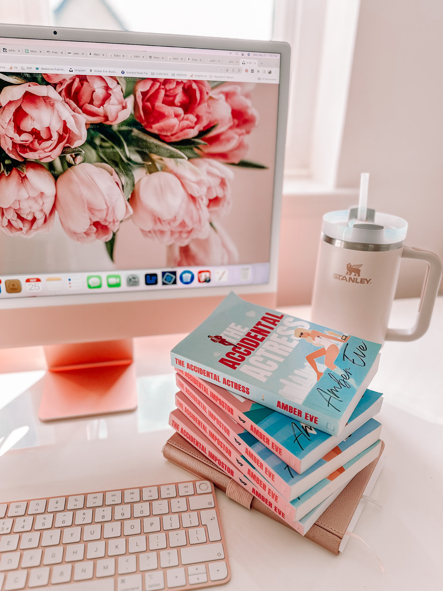 romcom books by Amber Eve next to pink iMac computer with floral desktop display